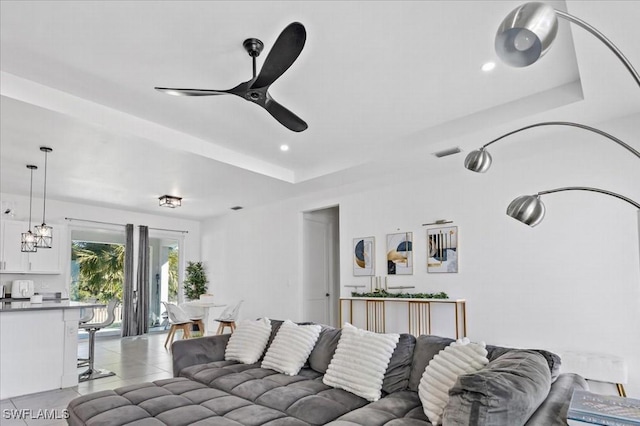 tiled living room with ceiling fan and a tray ceiling