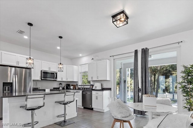 kitchen featuring pendant lighting, a center island, white cabinets, appliances with stainless steel finishes, and a breakfast bar area