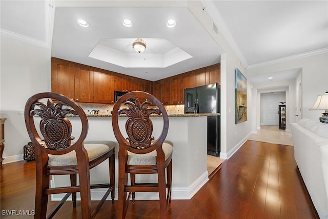 kitchen with light stone countertops, black fridge, dark hardwood / wood-style floors, backsplash, and crown molding