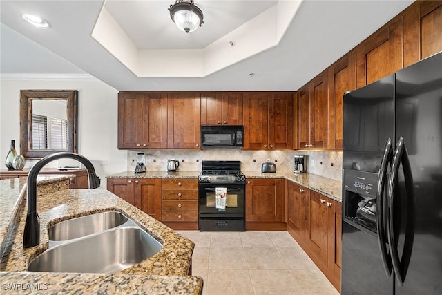 kitchen with a raised ceiling, light stone counters, sink, and black appliances