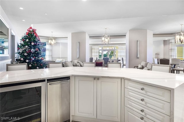 kitchen with pendant lighting, light stone counters, white cabinets, and beverage cooler