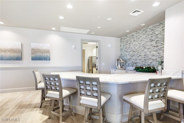 bar with stainless steel refrigerator, light stone counters, and light hardwood / wood-style flooring