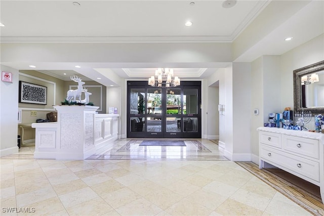 foyer entrance with a raised ceiling, ornamental molding, and a chandelier