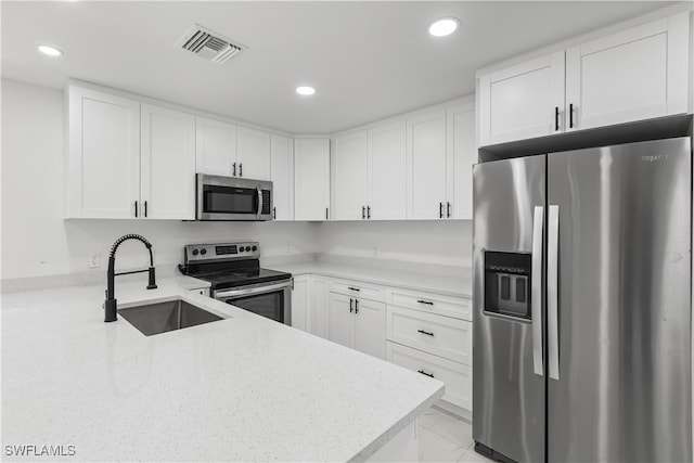 kitchen with white cabinets, sink, appliances with stainless steel finishes, light stone counters, and kitchen peninsula