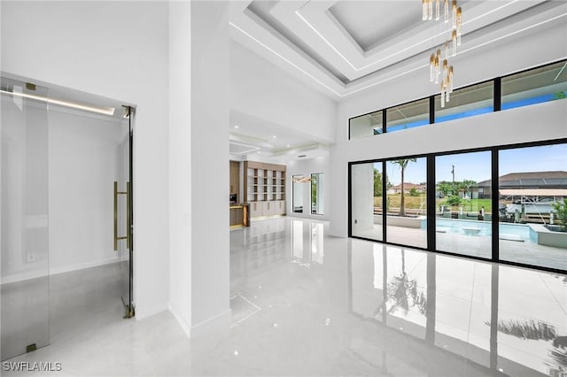 hall featuring french doors, a towering ceiling, a tray ceiling, and a notable chandelier