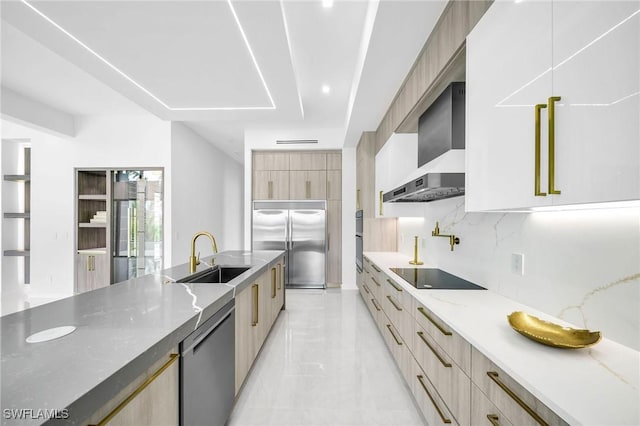 kitchen featuring decorative backsplash, appliances with stainless steel finishes, light stone counters, wall chimney exhaust hood, and sink