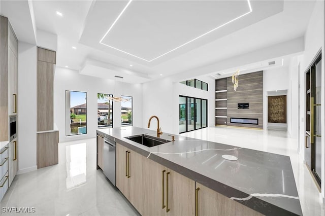 kitchen with light brown cabinets, a raised ceiling, sink, light stone countertops, and decorative light fixtures