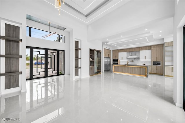 unfurnished living room featuring french doors, sink, a towering ceiling, a chandelier, and a tray ceiling