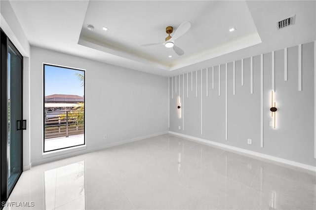 empty room with plenty of natural light, ceiling fan, and a raised ceiling