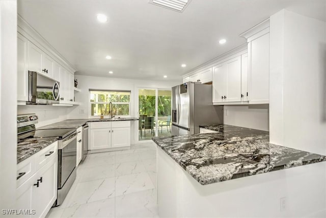 kitchen featuring kitchen peninsula, appliances with stainless steel finishes, sink, dark stone countertops, and white cabinetry