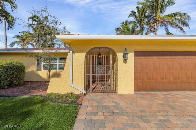 view of exterior entry featuring a garage, decorative driveway, and stucco siding