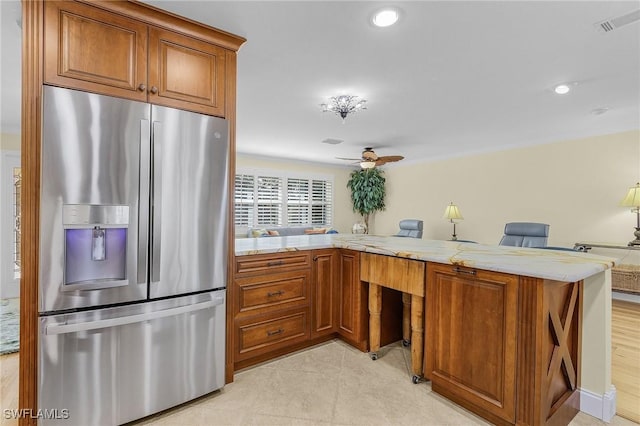 kitchen featuring kitchen peninsula, stainless steel refrigerator with ice dispenser, light stone countertops, a kitchen breakfast bar, and ceiling fan