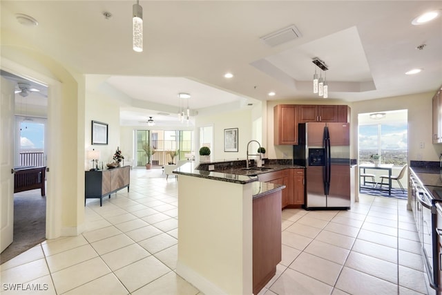 kitchen featuring a wealth of natural light, a raised ceiling, stainless steel fridge with ice dispenser, kitchen peninsula, and decorative light fixtures