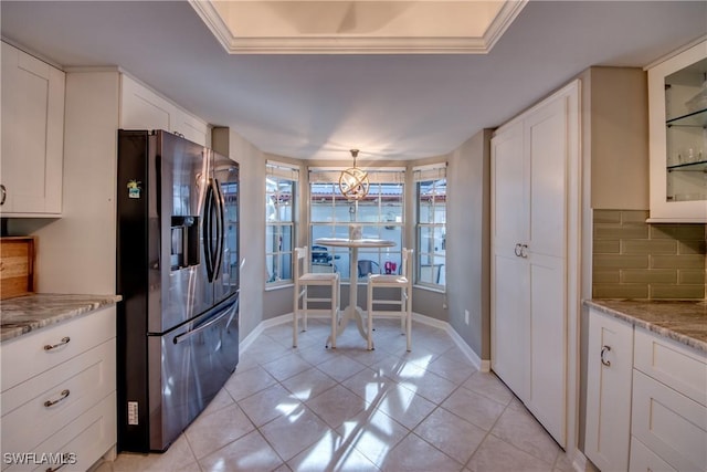 kitchen featuring white cabinetry, stainless steel fridge with ice dispenser, decorative backsplash, light tile patterned flooring, and ornamental molding