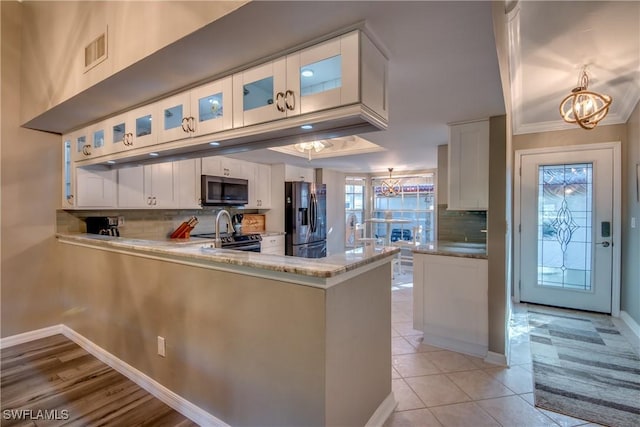 kitchen featuring white cabinetry, stainless steel appliances, an inviting chandelier, kitchen peninsula, and decorative backsplash