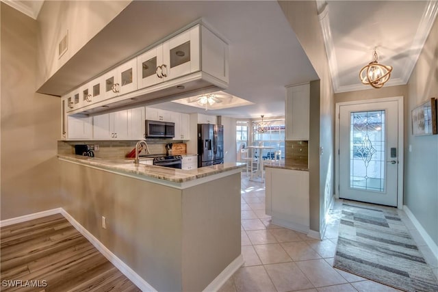 kitchen featuring tasteful backsplash, kitchen peninsula, a chandelier, white cabinets, and appliances with stainless steel finishes