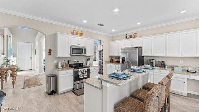 kitchen featuring white cabinets, appliances with stainless steel finishes, a center island with sink, and light stone countertops