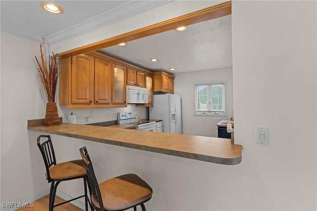 kitchen with hardwood / wood-style floors, a kitchen bar, white appliances, and crown molding