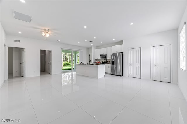 kitchen with a kitchen island with sink, ceiling fan, light tile patterned floors, white cabinetry, and stainless steel appliances