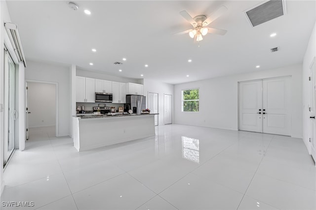 kitchen featuring a kitchen island with sink, white cabinets, ceiling fan, dark stone countertops, and stainless steel appliances