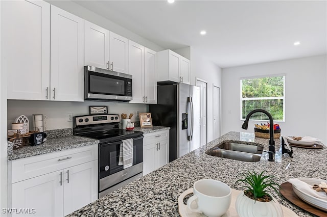 kitchen with white cabinets, appliances with stainless steel finishes, light stone counters, and sink