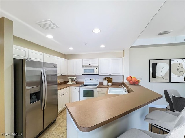 kitchen featuring visible vents, a breakfast bar, a peninsula, white appliances, and a sink