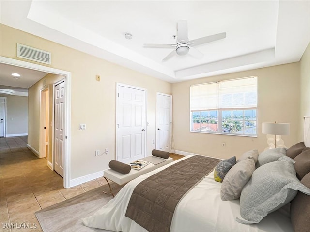 bedroom featuring visible vents, ceiling fan, baseboards, light tile patterned flooring, and a raised ceiling