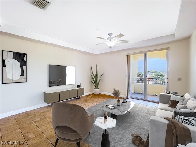 tiled living room with ceiling fan and a tray ceiling