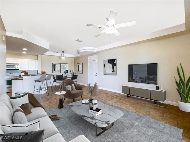 tiled living room with a tray ceiling and ceiling fan