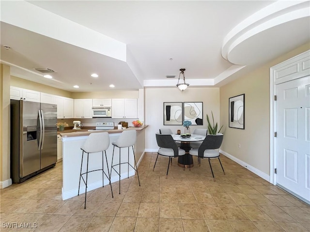 kitchen with stove, white cabinets, stainless steel refrigerator with ice dispenser, a tray ceiling, and decorative light fixtures