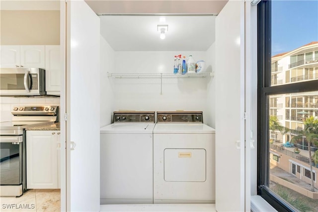 clothes washing area with washer and clothes dryer, a healthy amount of sunlight, and light tile patterned flooring