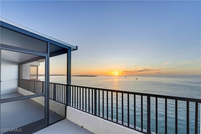 balcony at dusk featuring a water view