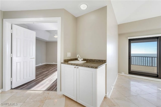 kitchen featuring sink, light tile patterned floors, white cabinets, dark stone counters, and a water view