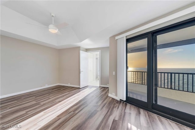 empty room with a raised ceiling, ceiling fan, a water view, and light wood-type flooring