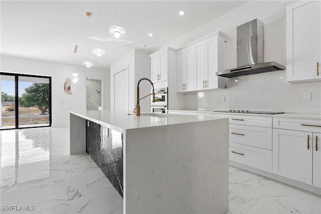 kitchen with white cabinetry, wall chimney exhaust hood, hanging light fixtures, black electric cooktop, and a center island with sink