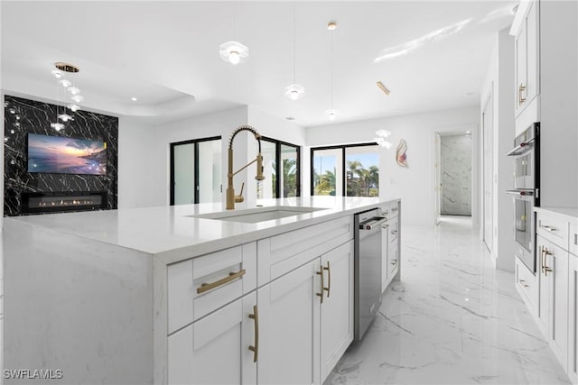 kitchen featuring stainless steel appliances, sink, a center island with sink, white cabinetry, and hanging light fixtures