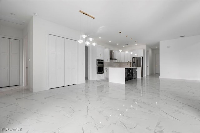 kitchen featuring pendant lighting, a center island with sink, wall chimney range hood, sink, and white cabinetry