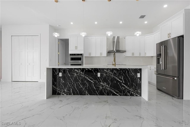 kitchen featuring wall chimney exhaust hood, decorative light fixtures, high quality fridge, a kitchen island with sink, and white cabinets