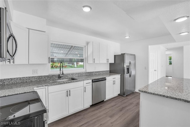 kitchen featuring light stone counters, dark wood-style flooring, stainless steel appliances, white cabinetry, and a sink