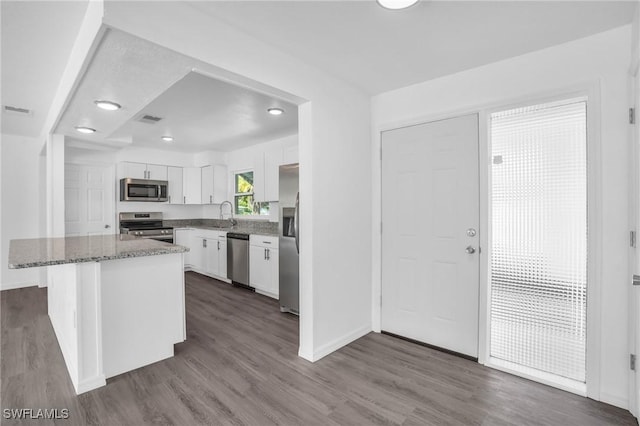 kitchen featuring light stone counters, stainless steel appliances, white cabinets, a kitchen island, and wood finished floors