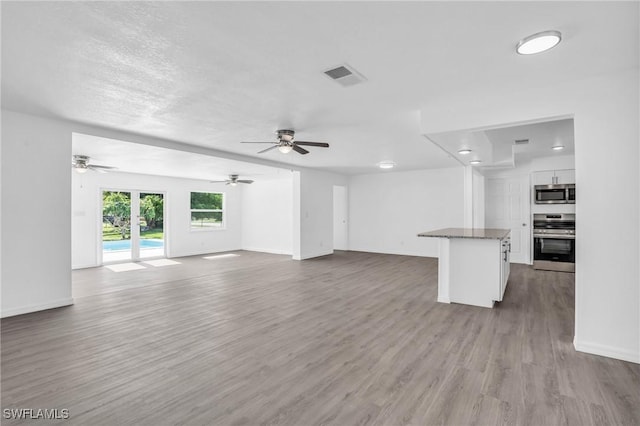 unfurnished living room with baseboards, visible vents, a textured ceiling, and light wood finished floors