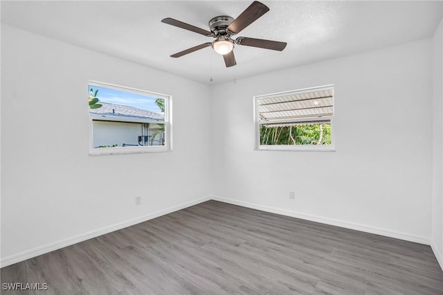 unfurnished room featuring a ceiling fan, baseboards, dark wood finished floors, and a wealth of natural light