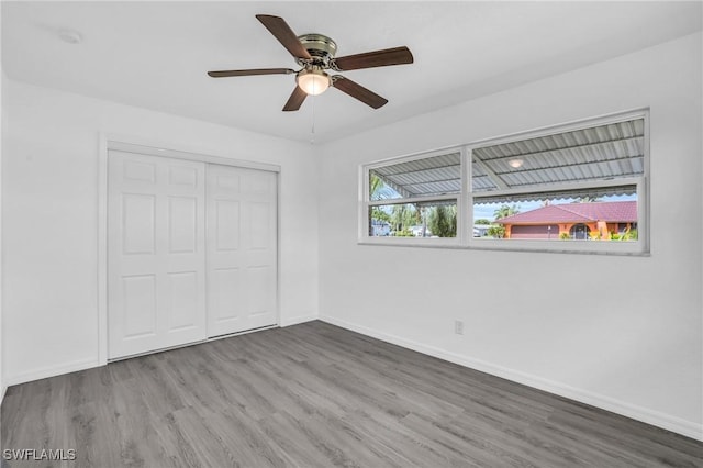 unfurnished bedroom featuring ceiling fan, a closet, wood finished floors, and baseboards