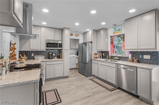 kitchen with stainless steel appliances, sink, washer / clothes dryer, wall chimney exhaust hood, and light wood-type flooring