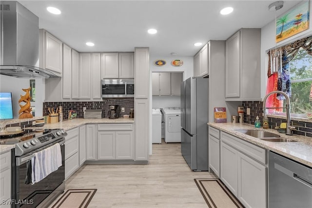 kitchen with stainless steel appliances, sink, washing machine and clothes dryer, light stone countertops, and wall chimney range hood