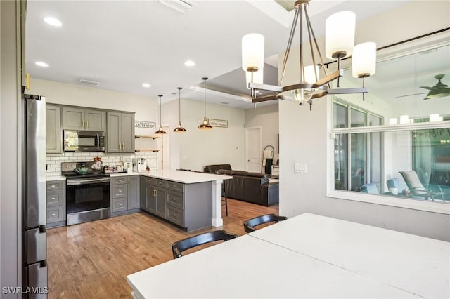 kitchen with kitchen peninsula, decorative light fixtures, gray cabinets, a breakfast bar, and appliances with stainless steel finishes