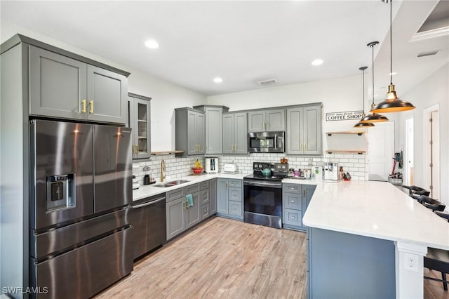 kitchen featuring a kitchen breakfast bar, sink, hanging light fixtures, kitchen peninsula, and stainless steel appliances