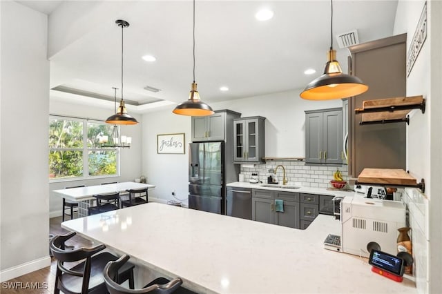 kitchen with stainless steel appliances, a raised ceiling, sink, gray cabinets, and hanging light fixtures