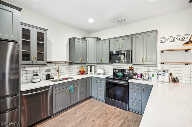 kitchen featuring light stone countertops, sink, backsplash, light hardwood / wood-style floors, and appliances with stainless steel finishes