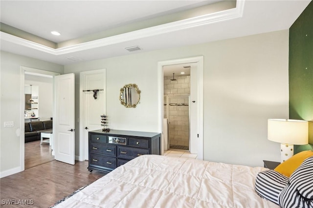 bedroom with ensuite bathroom, a raised ceiling, and hardwood / wood-style flooring